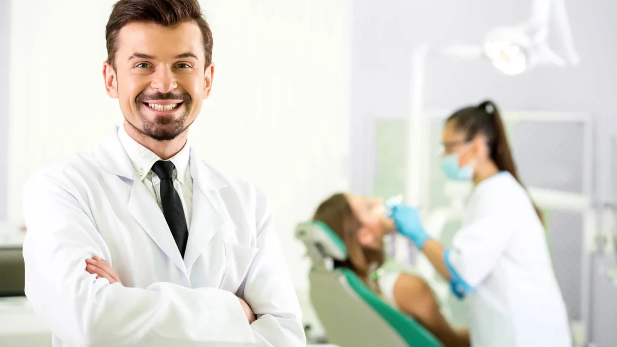 Smiling male professional dentist in Matthews, NC, with patient and doctor behind