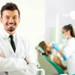 Smiling male professional dentist in Matthews, NC, with patient and doctor behind