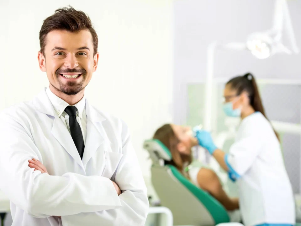 Smiling male professional dentist in Matthews, NC, with patient and doctor behind